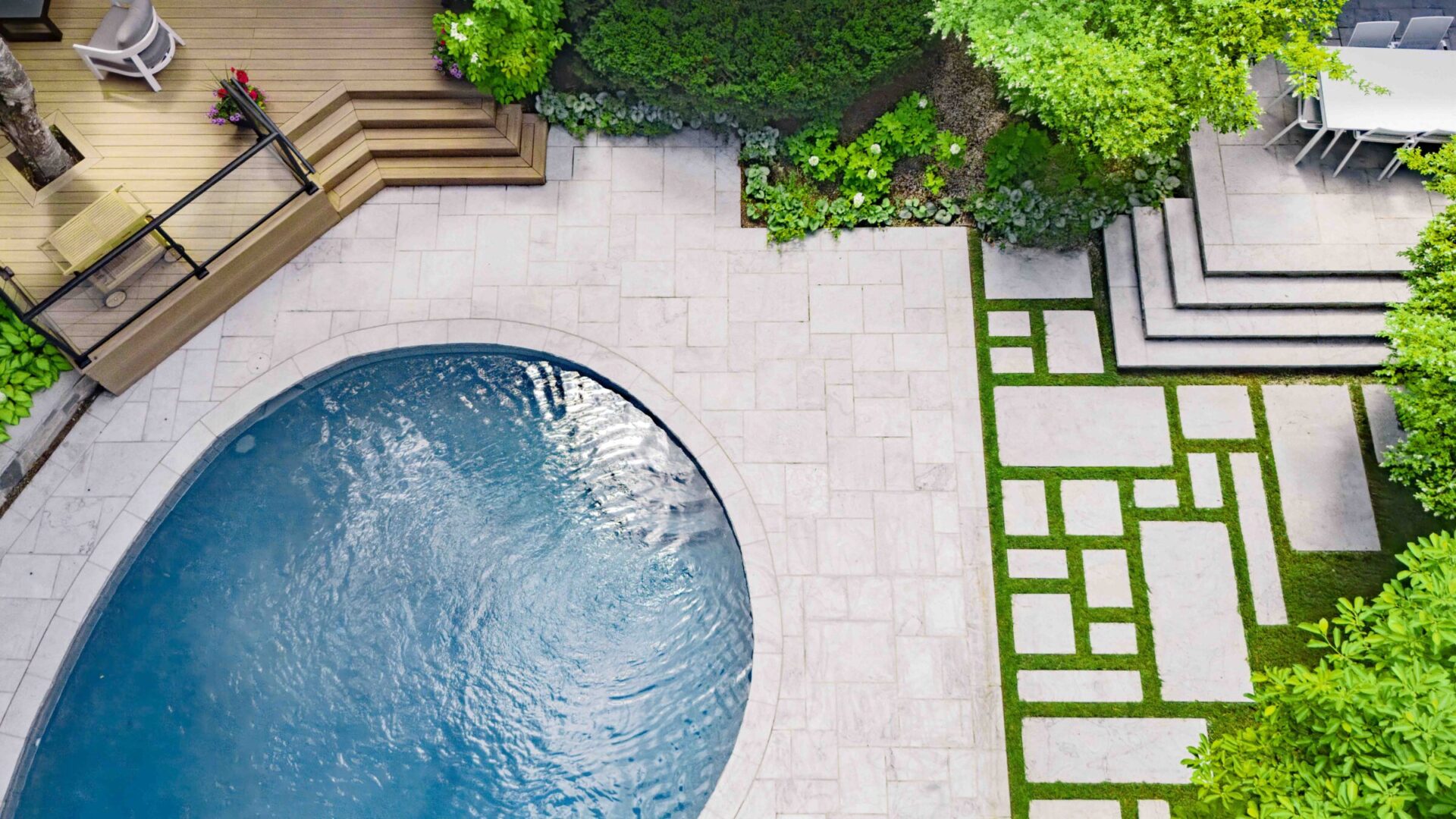 An aerial view of a backyard with a kidney-shaped pool, pavers, landscaping, dining area, and lounge chairs on a sunny day.