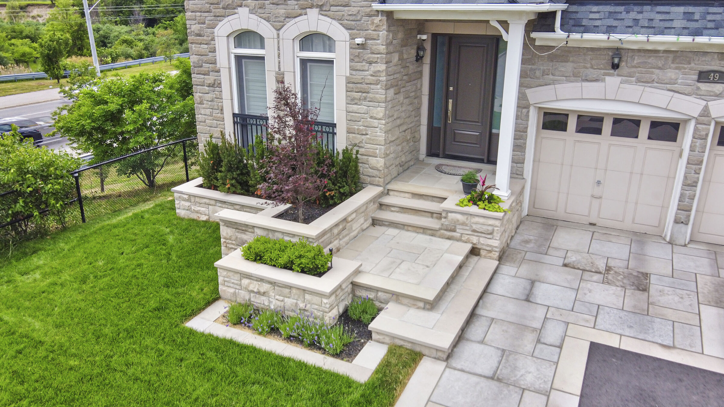 This image shows the exterior porch entry to a house house with stone facade, steps leading to a front door, and landscaped gardens.