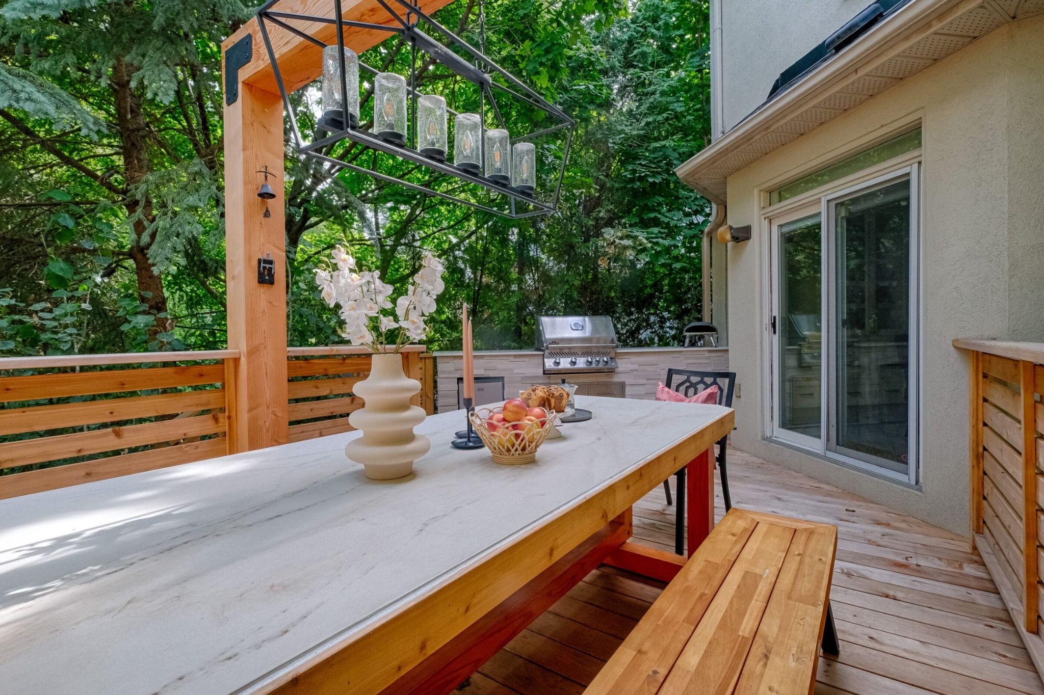 Cedar deck dining area with pendant light fixture, marble table, and counter with built-in grill and built-in undercounter fridge