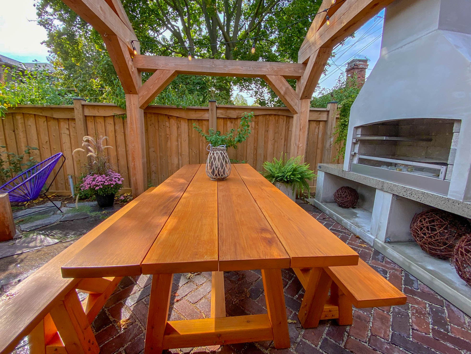 Cedar pergola with picnic table and outdoor wood-fired oven on brick patio