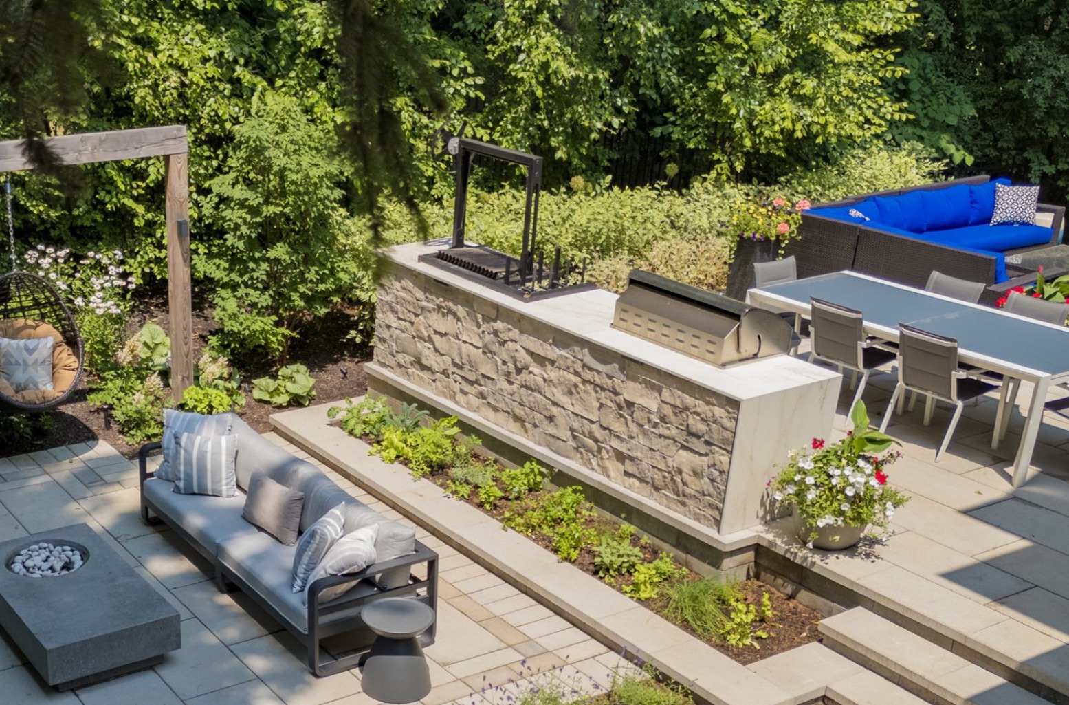 Overhead view of a luxury outdoor patio with a stone kitchen island, built-in grill, dining set, and fire pit lounge.