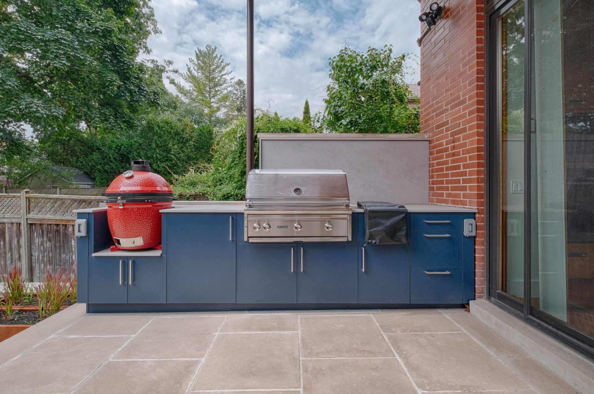 Urban Toronto backyard featuring stone patio and outdoor kitchen that includes kamado grill, built-in gas grill, and modern cabinetry.