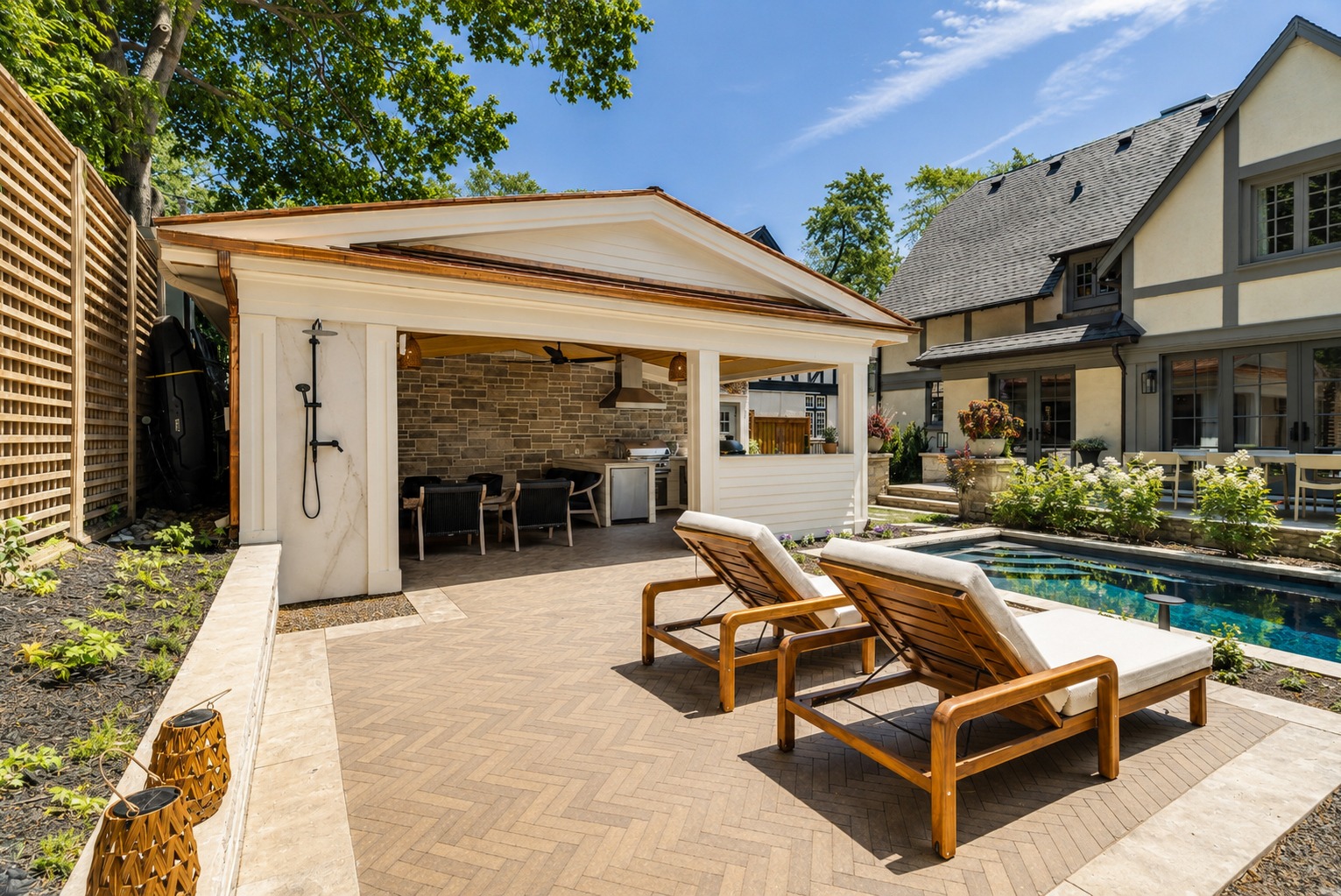 A modern outdoor kitchen next to a pool and deck chairs.